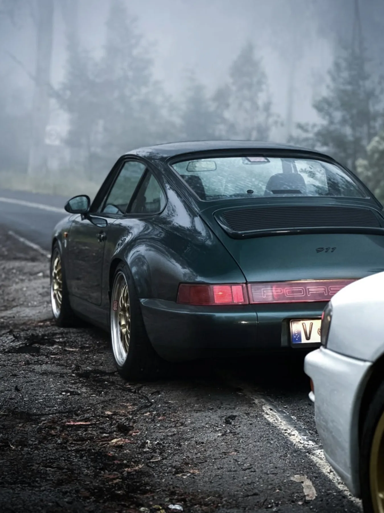 A dark green Porsche 911 on a misty forest road
